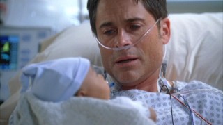 A recuperating Robert (Rob Lowe) holds his son Evan for the first time.