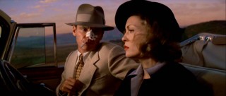 Jake and Evelyn strike a classic film noir pose while driving at sunset.