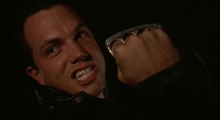 Cocky young thug Tate (Adam Baldwin) displays his brass knuckles as a threat to his young passenger.