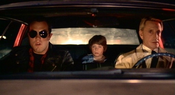 Tate (Adam Baldwin), Travis (Harley Cross), and Cohen (Roy Scheider) act cool as they slowly move through a highway police check point.