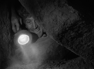 Charles Tatum (Kirk Douglas) shines a flashlight on a man trapped in an old Indian cave dwelling and tomb.