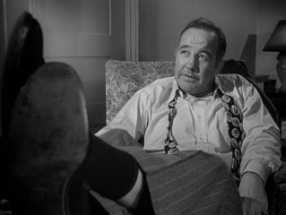 Now a big shot, Governor Willie Stark (Broderick Crawford) sits back and puts his feet up as he tells officials to write him an undated resignation letter.