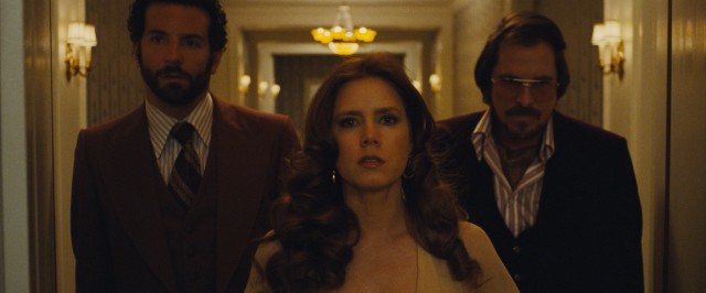 The title "American Hustle" is laid over this shot of Richie (Bradley Cooper), Sydney (Amy Adams), and Irving (Christian Bale) walking into an important meeting.