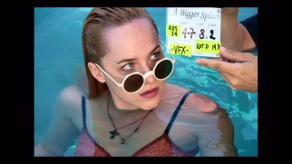 A slate is clapped right in front of Dakota Johnson's sunglassed face in a behind-the-scenes still from A Bigger Splash's photo gallery.