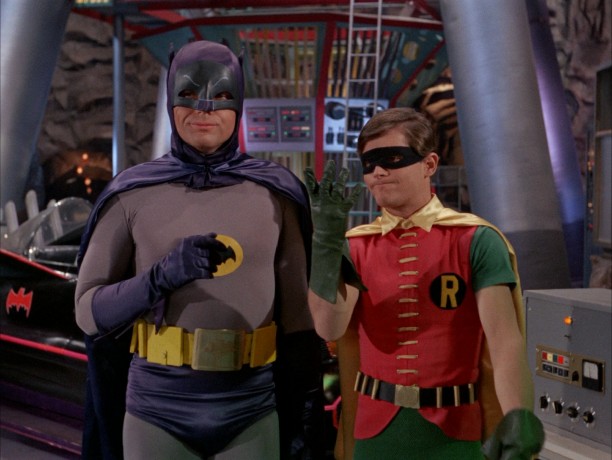 In the Batcave, in front of the Batmobile, Batman (Adam West) and Robin (Burt Ward) consider and count five Batclues.
