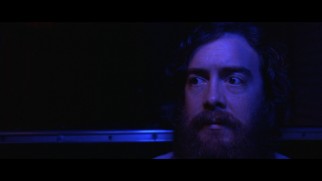 An amusement park's haunted house ride casts an eerie blue tint over Dwight's hairy face in this extended opening.