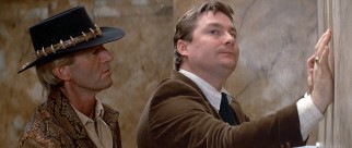 Crocodile Dundee (Paul Hogan) makes a DEA agent (Stephen Root in his film debut) uncomfortable at a urinal.