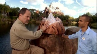 With his trademark big earring facing the attraction, veteran Imagineer Joe Rohde compares an Expedition Everest model to the mountain itself, pointing out design features that add to its presence.