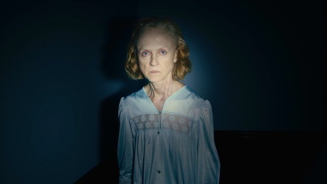 Deborah Logan (Jill Larson) does not look pleased to be filmed with a bright light in the dark.