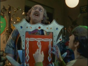 A horrified Tim watches as magic shop owner Mr. Malik (Harvey Atkin) has an accident with an unfortunately-placed guillotine.