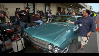 Two crew members take a measurement of the front of the Cadillac in which Tony drives Don.