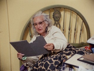 From bed, Edith "Big Edie" Beale looks at old pictures in a folder Little Edie has just ripped trying to take from her.