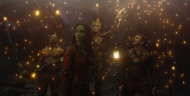 The Guardians of the Galaxy (Dave Bautista, Zoe Saldana, and Chris Pratt) marvel at the light generated by Groot.
