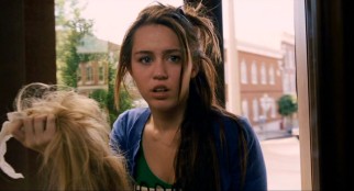 Miley Stewart moves through a revolving door with the metaphorical weight of her Hannah Montana wig in her hand.