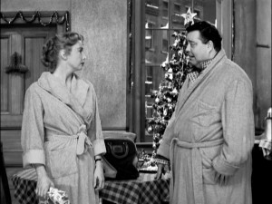 "Honeymooners" Alice (Audrey Meadows) and Ralph Kramden (Jackie Gleason) exchange gifts in front of their start-topped tree.