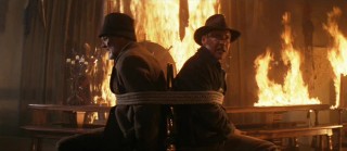 Two Dr. Joneses are feeling hot hot hot while tied together and surrounded by flames.