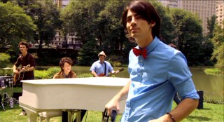 Joe Jonas rocks out with tambourine and red bow tie in the Brothers' Central Park music video "Love Is On Its Way."