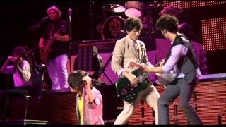 Nick and Kevin play with their guitars near one another while neon-shirted Joe rocks the mic in the bonus song "Shelf."