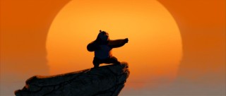 Atop a cliff against an orange sunset sky, Po strikes an iconic kung fu panda pose.