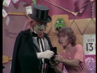 Mark (Butch Patrick) shows off his wallet family snapshots to Lidsville's Horatio J. HooDoo (Charles Nelson Reilly), turning the gears of the rotten magician's ransom plan.