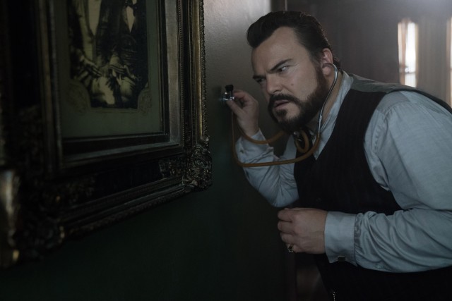 Jonathan Barnavelt (Jack Black) uses a stethoscope to listen to the clock inside the walls of his house in "The House with a Clock in Its Walls."