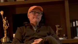 Director Barry Levinson sits casually in front of some awards in his featurette interview.