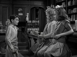 In the original black and white, Little George (Bobbie Anderson) serves Little Violet (Jeanine Anne Roose) and Little Mary (Jean Gale) candy in gray dresses.