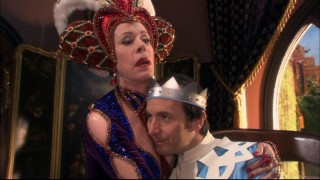 The control freak Queen Aggravain (Carol Burnett) comforts her middle-aged bachelor son, Prince Dauntless (Dennis O'Hare) with a little bitty.