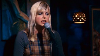 Anna Faris plays Nora Farrington, a coffee house cashier and aspiring singer-songwriter who shares her brand name-filled protest songs every Saturday night.
