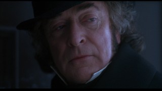 After a song establishes his not-so-great reputation, Michael Caine makes his first clear appearance as miserly protagonist Ebenezer Scrooge.