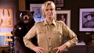 In front of a stuffed bear and transgendered Photoshop jobs, Miss Hulka (Jane Lynch) of Hulka's Rock stands proudly.