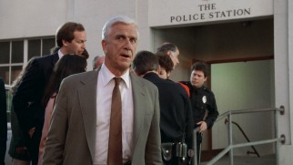 Lieutenant Frank Drebin (Leslie Nielsen) plays it cool after being responsible for his car's downhill roll.