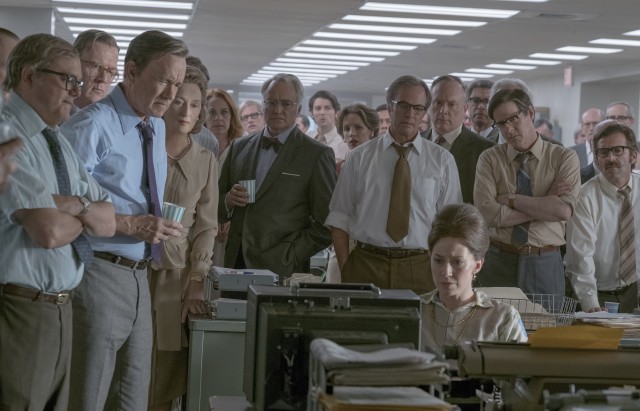 Ben Bradlee (Tom Hanks) and his Washington Post reporters gather around to watch a television news report on actions taken against The New York Times.