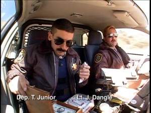 Sunglasses, mustaches, and Coconut Nut Clusters. With dashboard cameras, we often venture into on-duty patrol cars like this one transporting Deputy Travis Junior (Robert Ben Garant) and Lt. Dangle.