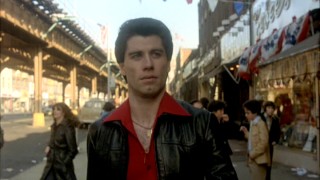 In the iconic, oft-parodied opening of "Saturday Night Fever", Tony Manero (John Travolta) struts along on the sidewalk to the Bee Gees' "Stayin' Alive", carrying a paint can and eating two stacked slices of pizza.