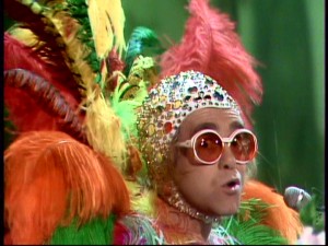No need to adjust your television. Elton John merely brings out all the bright colors and glitzy wardrobe touches.