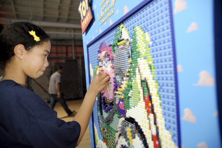 A girl works on filling in Buzz's face with pink Lego pieces.