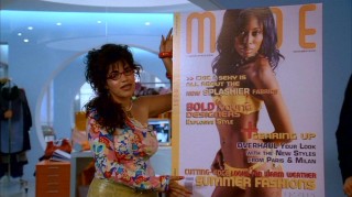 Betty presents a magazine cover during a business meeting, but all eyes are on her distinctive Queens makeover.