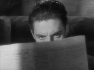 Hannay (Robert Donat) learns that he is wanted for murder from a fellow train passenger's newspaper.