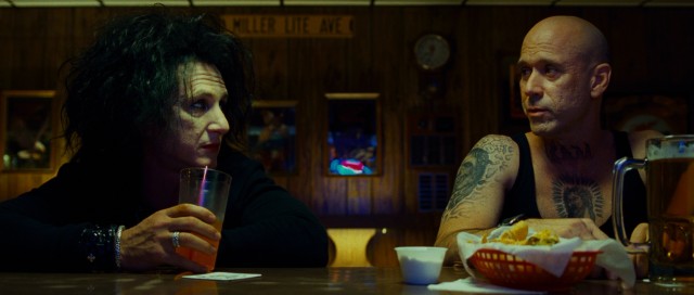 While sipping a soft drink at a bar, Cheyenne (Sean Penn) shares a conversation with a tattoo artist (Gordon Michaels).