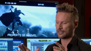 Composer Brian Tyler discusses his "Dark World" score in front of a freeze frame from the film and many computer screens.