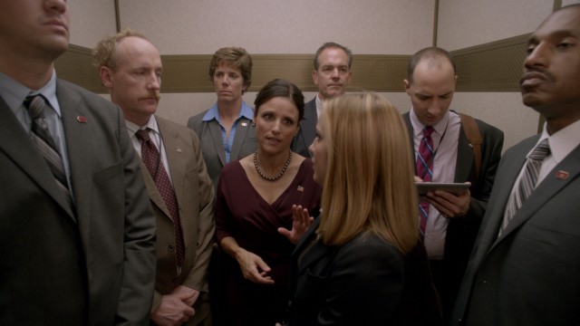 Flanked by secret service, Selina Meyer (Julia Louis-Dreyfus) continues to consult staffers (Matt Walsh, Anna Chlumsky, and Tony Hale) on an elevator ride to a public function.