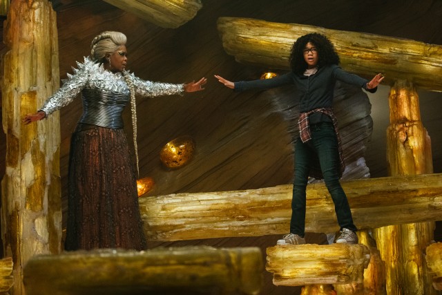 A normal-sized Mrs. Which (Oprah Winfrey) stands in support next to Meg (Storm Reid) as they consult the cave sage Happy Medium.