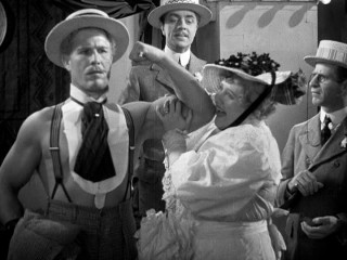 Rocking a dickie and suspenders look, standout supporting character Eugen Sandow (Nat Pendleton) allows his biceps to be felt by a visibly impressed wife, to the puzzlement of her husband and to the advancement of Florenz Ziegfeld.