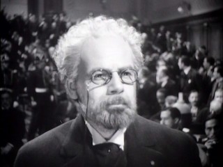 While the courtroom breaks out in discussions, old Emile Zola (Paul Muni) remains stoically unmoved by the verdict he's just been handed.