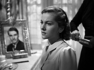 The increasingly concerned second Mrs. de Winter (Joan Fontaine) has her hair brushed while a photographed Larry Olivier watches.