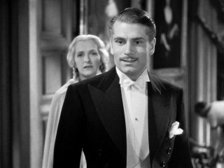 Maxim (Laurence Olivier) is less than happy with his new wife's party dress choice.